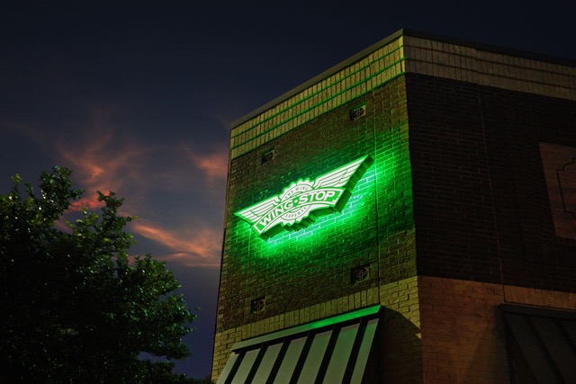 A Wingstop restaurant at dusk with its green sign lit